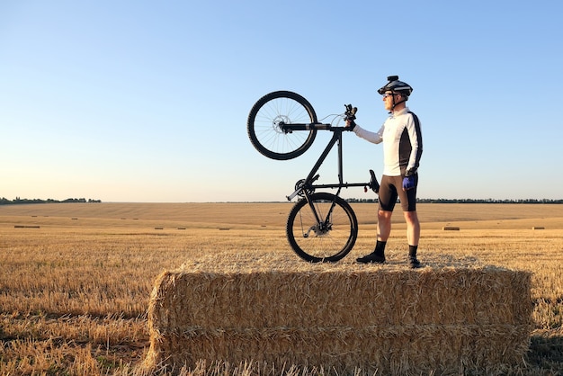 Cycliste avec le vélo reposant sur le champ moissonné de paille