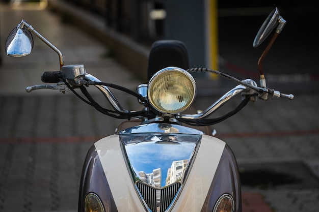 Un cyclomoteur de moto blanc rétro se trouve dans un parking sur fond de vue de face de mur gris