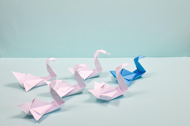 Cygnes en papier Origami sur fond bleu Concept de leadership Un cygne bleu mène un troupeau de cygnes blancs