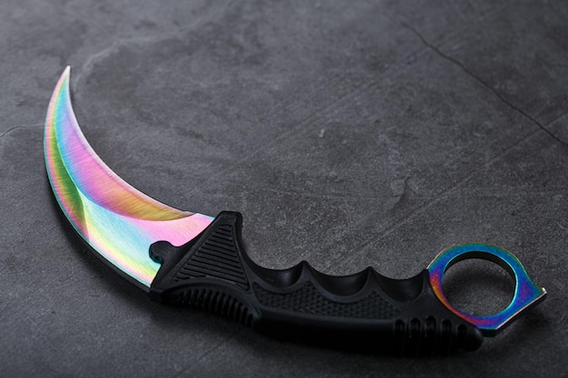 Photo dague kerambit avec une lame de couleur arc-en-ciel sur un fond texturé sombre. armes froides, espace libre