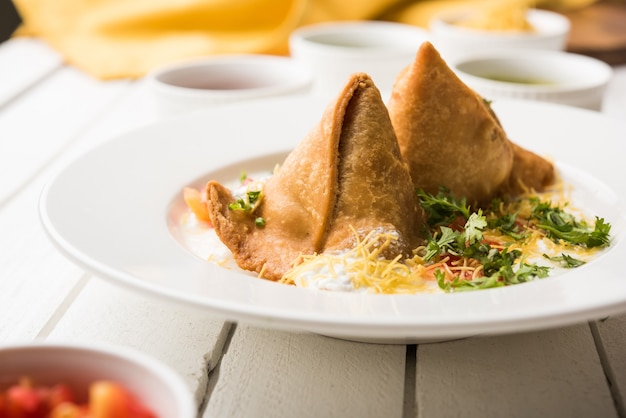 Photo dahi samosa ou samosa est une collation populaire de l'inde du nord trempée dans du lait caillé, de la malbouffe préférée à l'heure du thé servie avec du chutney de tamarin et de menthe ou du ketchup aux tomates et du piment vert frit