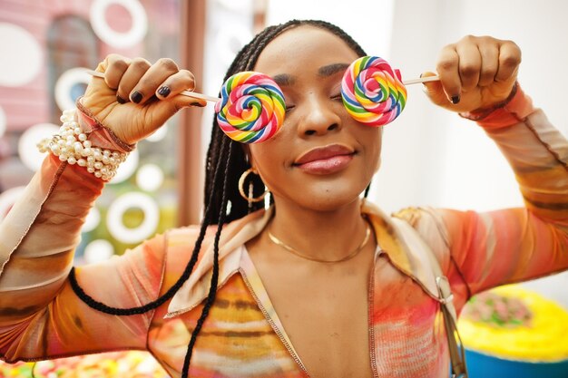 Une dame afro-américaine du millénaire au magasin de bonbons avec des sucettes se couvre les yeux