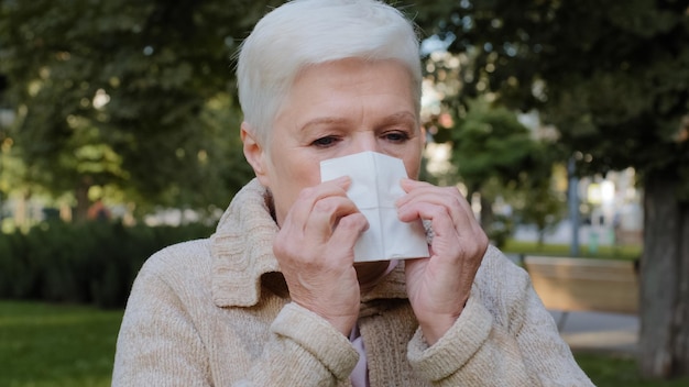 Dame d'âge moyen allergique se sent mal ayant un symptôme de la grippe malade vieille femme mûre tenir des éternuements de tissu a de la fièvre attrapé froid soufflant nez qui coule dans un mouchoir malade concept d'allergie vue rapprochée