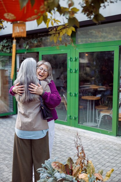 Une dame âgée joyeuse en veste chaude embrasse le meilleur ami aux cheveux longs se réunissant dans la rue de la ville