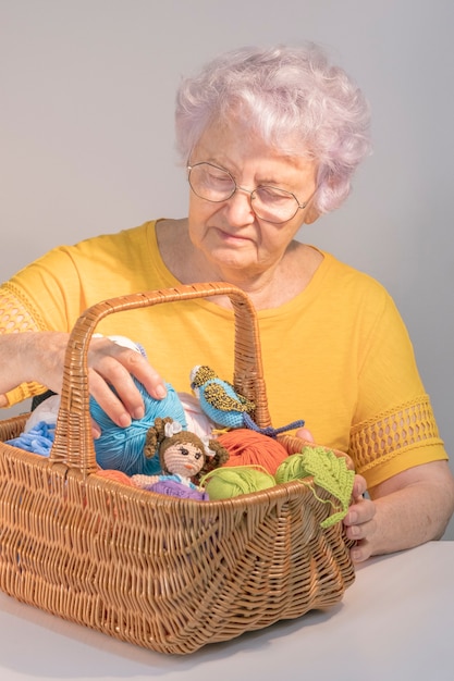 Photo une dame âgée avec un panier avec des pelotes de laine et des jouets tricotés. concept d'artisanat et de bricolage. passe-temps féminin.