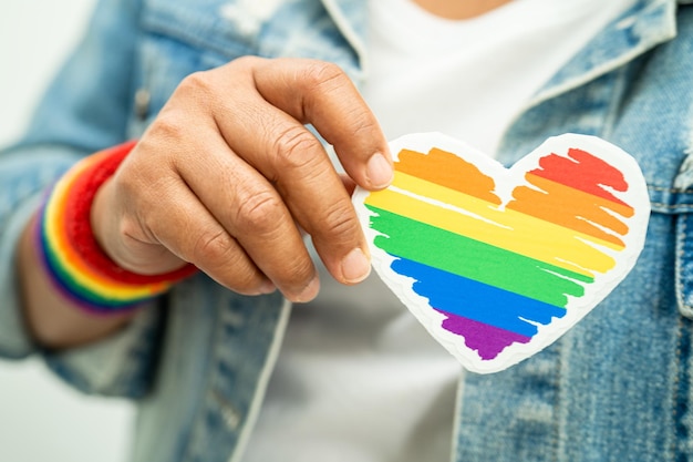 Une dame asiatique portant des bracelets avec un drapeau arc-en-ciel et tenant le cœur rouge, symbole du mois de la fierté LGBT, célèbre chaque année en juin les droits de l'homme des gays, lesbiennes, bisexuels, transgenres