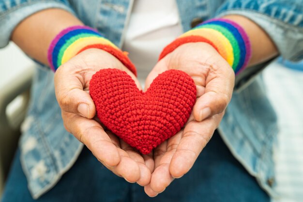 Une dame asiatique portant des bracelets de drapeau arc-en-ciel et tenant le symbole du coeur rouge du mois de la fierté LGBT célèbre chaque année en juin la société des droits de l'homme transgenres bisexuels lesbiennes gays