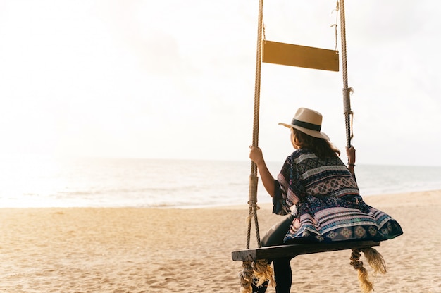 Dame assise sur une balançoire en bois et regardant la plage