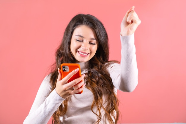 Une dame aux cheveux longs avec une expression amusée lit un message sur la victoire à la loterie sur le téléphone. Une femme regarde la victoire.