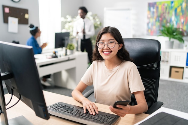 Dame avec une beauté asiatique distinctive travaille dans un bureau à un poste de travail informatique à la recherche d'un client