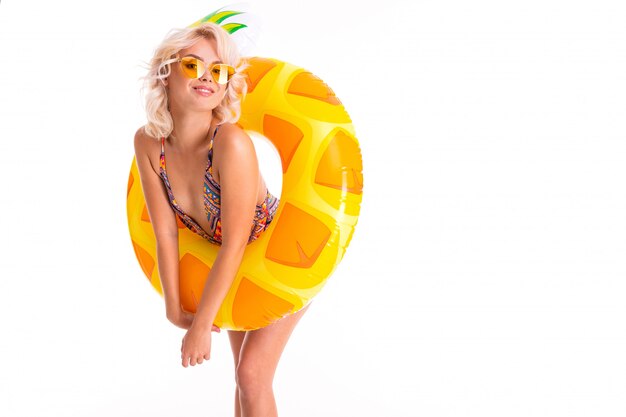 Dame blonde douce en maillot de bain avec ananas cercle de natation sur blanc