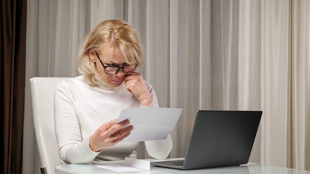 Une dame blonde lit une lettre avec de mauvaises nouvelles et se sent stressée