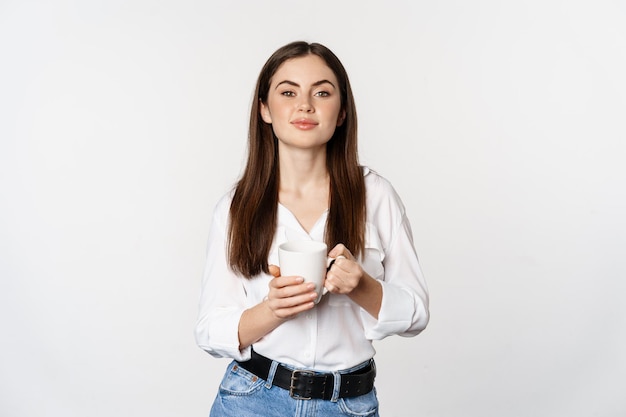 Dame de bureau jeune femme d'affaires moder tenant une tasse avec du thé au café et souriant debout contre la Pentecôte...