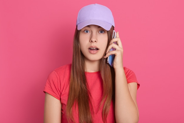 Dame en casquette de baseball et t-shirt rouge parlant par téléphone avec une expression faciale étonnée