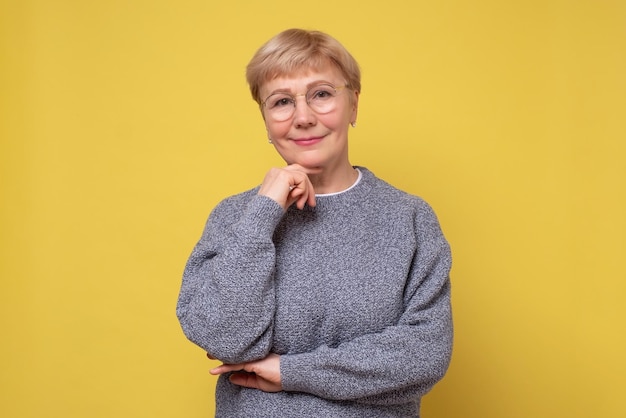 Dame caucasienne âgée avec des lunettes posant devant la caméra en souriant