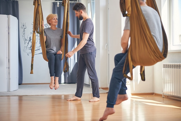 Dame caucasienne blonde aux pieds nus avec une coupe de cheveux courte regardant son professeur sérieux de yoga aérien