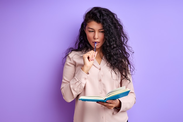 Dame en chemisier se tenir dans ses pensées avec cahier en mains, femme brune bouclée prendre des notes