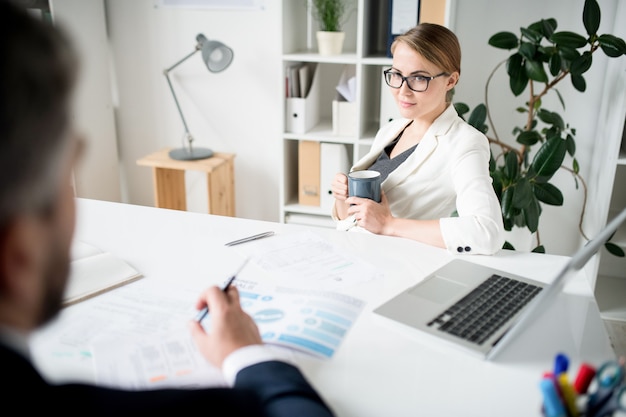 Dame confiante avec mug parler à un conseiller financier au bureau