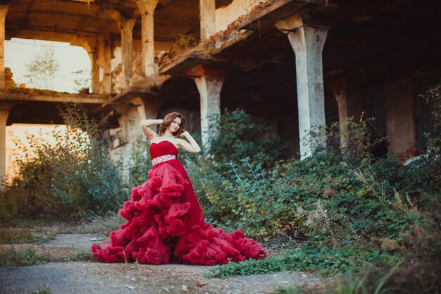 Dame dans une longue robe rose luxuriante de luxe en plein air. Femme en robe nuageuse rouge - symbole de beauté et de renouveau de la société