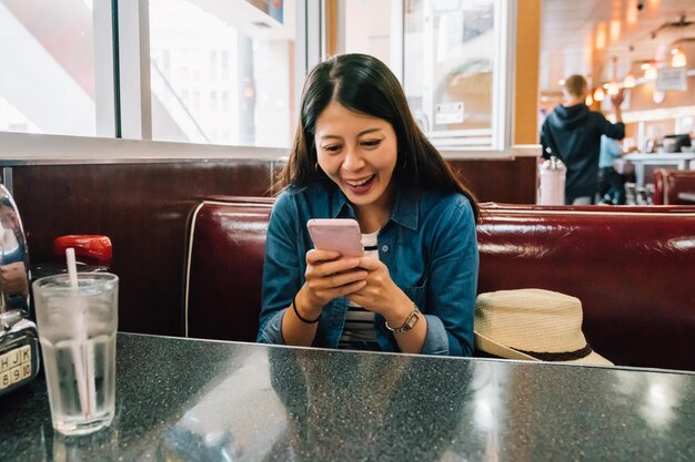 dame décontractée se détendant assise dans le restaurant et discutant joyeusement avec son amie par smartphone en attendant le repas. jeune femme utilisant joyeusement le téléphone portable. Concept de déjeuner asiatique.