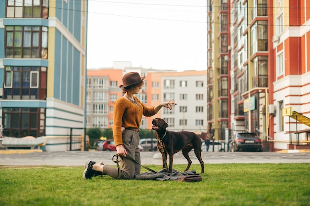 Dame élégante au chapeau jouant avec un chien ludique sur l'herbe