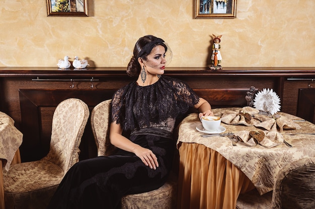 Une dame élégante dans une robe de soirée à une table dans un café. Intérieur du restaurant.