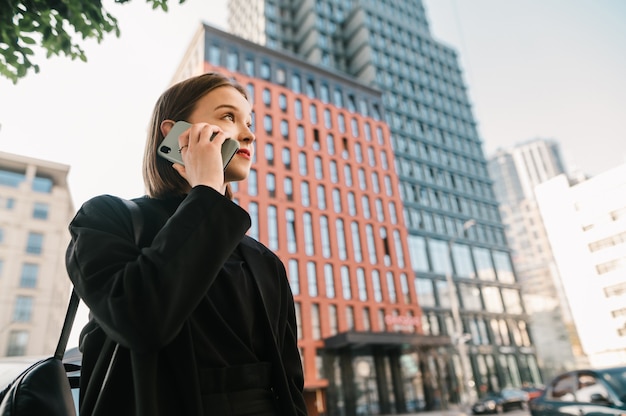 Dame élégante en vêtements sombres se dresse contre l'architecture moderne