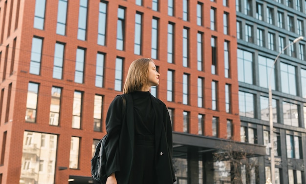 Dame élégante en vêtements sombres se dresse contre l'architecture moderne