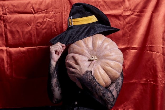 Photo dame d'halloween portant une tasse de sorcière et tenant une grosse citrouille d'halloween une femme au chapeau de sorcière et sanctifier...