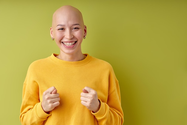 Dame heureuse chauve en chemise jaune montrant le geste de la figue, vous ne l'obtenez pas de toute façon. Le langage du corps. Signe de refus de figue. Jeune femme adulte à l'intérieur studio isolé sur fond de mur vert, espace copie