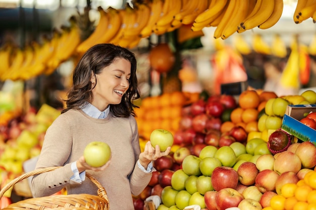 Une dame heureuse avec un panier entre les mains choisit des pommes fraîches biologiques au marché