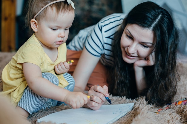 Photo dame joyeuse apprenant à son enfant à dessiner et souriant tout en tenant un crayon