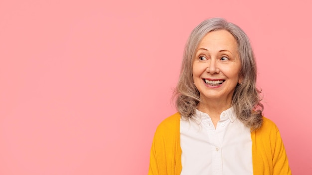 Une dame mature qui regarde de côté intéressée par l'espace vide studio rose