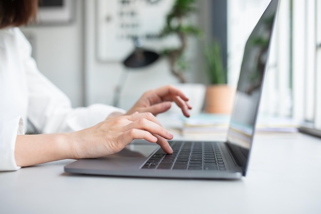 Dame méconnaissable travaillant avec un ordinateur portable et tapant sur un clavier d'ordinateur assis dans un espace de coworking