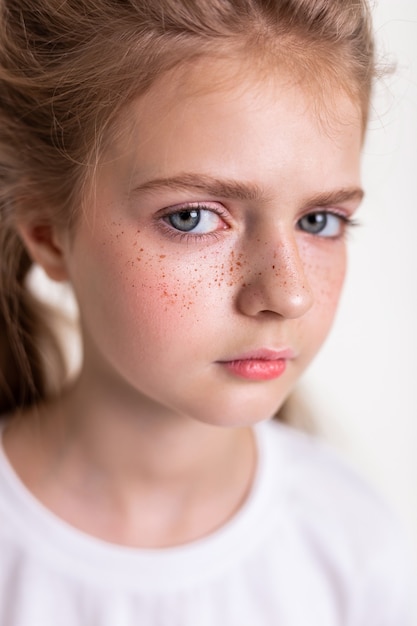 Dame mignonne sceptique. Séduisante jeune fille aux cheveux clairs regardant de côté avec de grands yeux bleus tout en ayant des taches de rousseur rouges