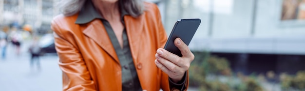 Dame mûre avec un téléphone portable vérifie le prix du scooter électrique à coup de pied dans la rue de la ville