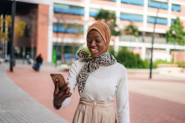 Dame musulmane noire souriante vérifiant le message sur smartphone