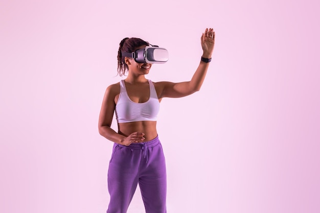 Dame noire excitée s'amusant avec la technologie 3D portant un casque de réalité virtuelle sur fond néon rose