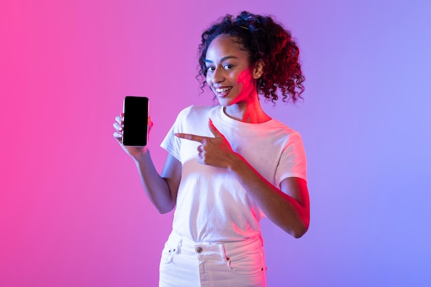 Une dame noire heureuse montrant son smartphone sur un fond rose et violet vibrant