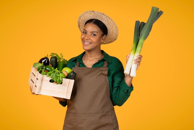 Dame noire tenant poireau et boîte avec fond jaune de légumes