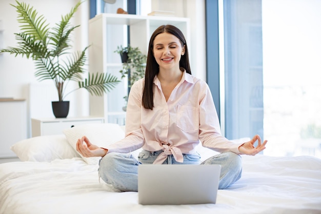 Une dame paisible assise en position de lotus pendant un cours en ligne en utilisant un ordinateur portable moderne