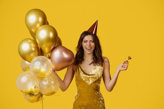Dame ravie avec une casquette d'anniversaire de ballons festifs et un ventilateur de fête célébrant une occasion spéciale sur fond jaune