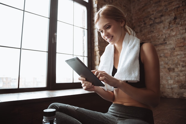 Dame de remise en forme avec une serviette assis dans une salle de sport tout en utilisant une tablette