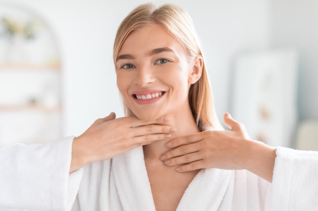 La dame s'occupe de sa peau en touchant délicatement le cou dans la salle de bain.