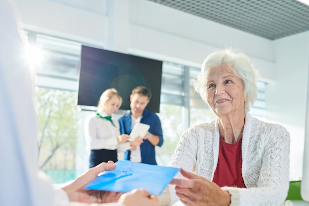 Dame senior positive recevant une enveloppe avec des documents en banque