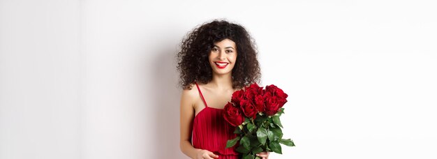 Dame souriante élégante avec des lèvres rouges et robe tenant un bouquet de roses et à la zone blanche heureuse