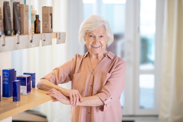 Dame souriante. Femme aux cheveux gris dans un chemisier beige à la recherche positive et souriante