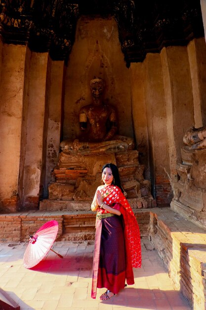 Photo une dame thaïlandaise en costume thaïlandais sourit et joignit les mains pour saluer l'ancien temple bouddhiste