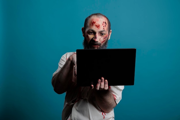 Dangereux monstre d'halloween naviguant sur Internet sur un ordinateur portable devant la caméra, tenant un ordinateur et étant effrayant et effrayant apocalyptique. Zombie maléfique effrayant de morts-vivants utilisant un ordinateur avec les médias sociaux.