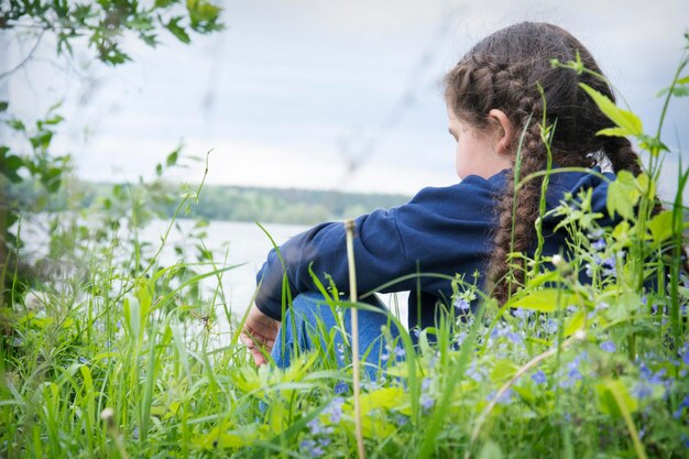 Photo dans l'après-midi d'été sur la rive du fleuve, une fille est assise dans les hautes herbes